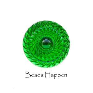 May include: A green glass button with a swirl design and a smaller green glass circle in the center. The button has a raised edge and a smooth surface.