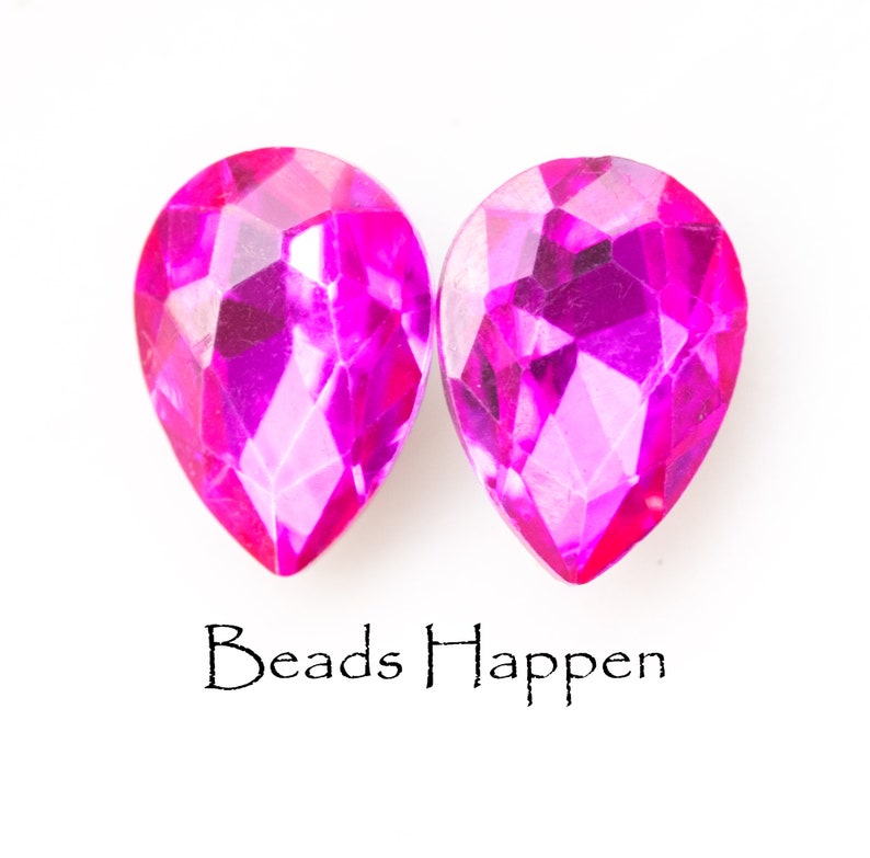 Puede incluir: Dos cuentas de vidrio de color rosa en forma de l&aacute;grima con un dise&ntilde;o facetado. Las cuentas est&aacute;n sobre un fondo blanco con el texto "Beads Happen" debajo.