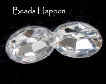 May include: Two clear glass oval-shaped beads with faceted edges. The beads are on a black background.
