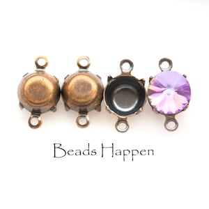 May include: Four antique gold-toned metal bead caps with three loops each. The bead caps are arranged in a row. The last bead cap has a purple iridescent crystal in the center. The text "Beads Happen" is printed below the bead caps.