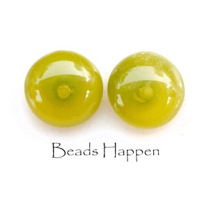 May include: Two round, olive-green glass beads with a central indentation. The beads have a glossy finish and are set against a white background. The text "Beads Happen" is written in black script below the beads.