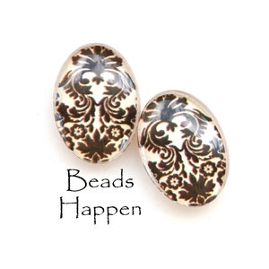 Peut inclure: Deux perles de verre ovales avec un motif damassé noir et blanc. Les perles sont sur un fond blanc avec le texte "Beads Happen" en dessous.