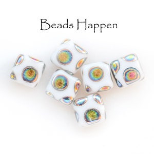 May include: Six white square beads with iridescent gold and rainbow accents. The beads have a speckled pattern and are arranged in a cluster on a white background. The text "Beads Happen" is written in black above the beads.