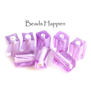 May include: A collection of seven translucent purple square beads with a white cylindrical core and a central hole. The text "Beads Happen" is printed in black above the beads. Each bead features a smooth, glossy finish and a distinct geometric shape.
