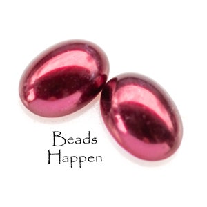 Puede incluir: Dos cuentas ovaladas de color burdeos con un acabado brillante. Las cuentas están sobre un fondo blanco.