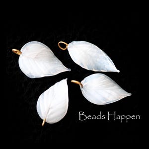 May include: Four white glass leaf-shaped charms with gold jump rings. The charms have a textured, frosted finish.
