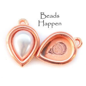 May include: Two copper teardrop-shaped pendant settings, one with a white pearl bead inside and the other empty. The text "Beads Happen" is printed above the settings.