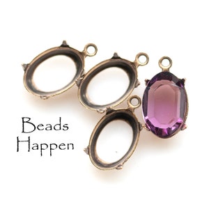 May include: Three antique gold oval-shaped metal settings with a single purple glass cabochon in the center. The settings have a loop at the top for hanging.
