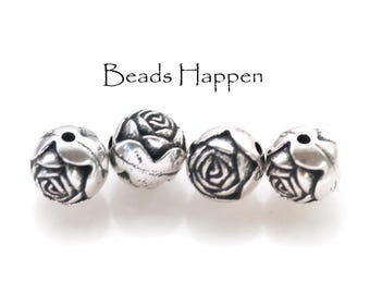 May include: Four silver beads with a rose design. The beads are round and have a detailed rose pattern.