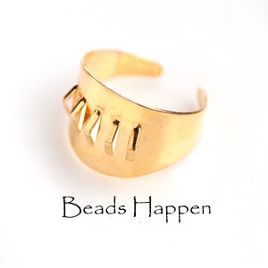 May include: Gold ring with a geometric design. The ring is made of metal and has a smooth finish. The design features a series of vertical lines and triangles.
