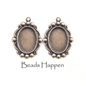 May include: Two antique silver-toned oval pendant settings with decorative beaded edges and a loop at the top. The text "Beads Happen" is printed in black below the pendants.