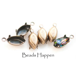 May include: Close-up of several antique brass-colored marquise-shaped jewelry settings, some empty, others with a faceted iridescent gemstone. The settings have a loop for attaching to a chain or other jewelry component. The text "Beads Happen" is at the bottom.