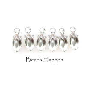 May include: Six silver-toned metal jewelry settings with a marquise-shaped bezel and a small circular loop at the top for attachment. The text "Beads Happen" is printed in black below the row of metal components against a plain white background.