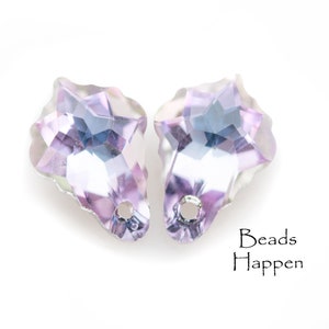 以下が含まれることがあります： 穴の開いた、星型の、虹色のファセットクリスタルビーズ2個。クリスタルは、青と銀のヒントを持つ、薄い紫色の色合いをしています。「Beads Happen」の文字が右下にあります。