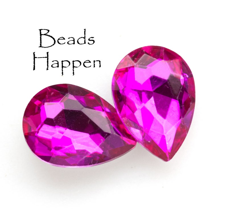 Puede incluir: Dos cuentas de vidrio de color rosa en forma de l&aacute;grima con un dise&ntilde;o facetado. Las cuentas est&aacute;n sobre un fondo blanco. El texto "Beads Happen" est&aacute; escrito encima de las cuentas.