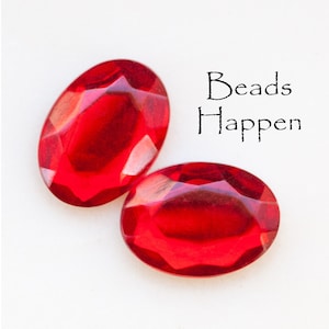 May include: Two red oval-shaped glass beads with a faceted design. The text "Beads Happen" is written in black on a white background.