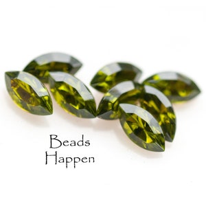 May include: A group of eight marquise-shaped green glass beads. The beads are faceted and have a shiny finish. The beads are arranged in a semi-circle on a white surface. The text "Beads Happen" is written below the beads.