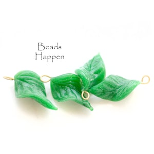 May include: Three green glass leaf-shaped beads with gold wire loops. The beads have a textured surface and are perfect for jewelry making.