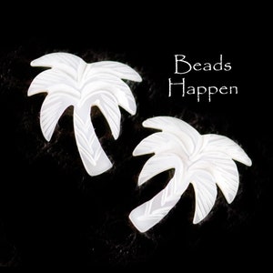 Könnte beinhalten: Zwei weiße, palmenförmige Perlen mit einem geschnitzten Design. Die Perlen befinden sich auf einem schwarzen Hintergrund.