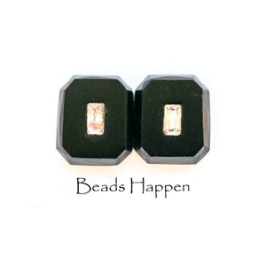 May include: Two black square-shaped display boxes with a clear rectangular gemstone in each. The boxes are side-by-side and the text "Beads Happen" is below them.