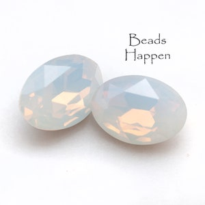 May include: Two iridescent white oval-shaped beads with a faceted design. The beads are on a white background.