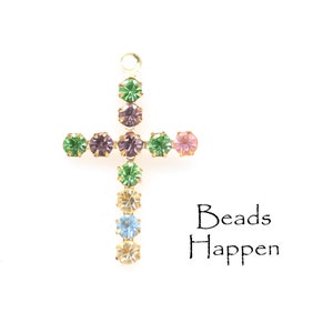 May include: A gold cross charm with colorful rhinestones. The cross is decorated with green, purple, pink, and blue rhinestones. The text "Beads Happen" is printed below the cross.