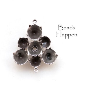 May include: Silver-toned metal pendant with six round cup settings for stones or beads. The pendant has a loop at the top for attaching to a chain or cord. "Beads Happen" is written in black text on a white background.