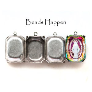 May include: Four silver-toned metal settings for bezel settings. The settings are rectangular with rounded corners. The setting on the right has a colorful iridescent glass cabochon with a white image of the Virgin Mary inside.