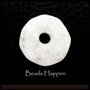 May include: White round bead with a hole in the center. The bead has a marbled effect and is about 1 inch in diameter. The bead is on a black background with the text "Beads Happen" below it.