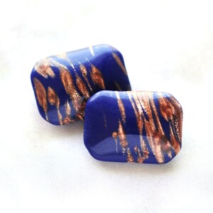 May include: A pair of blue and gold rectangular earrings with a marbled pattern.