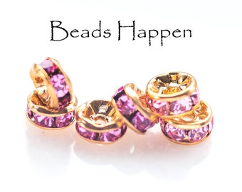 May include: Five gold-toned bead caps with pink crystal accents. The bead caps are stacked on a white surface. The text "Beads Happen" is visible above the bead caps.