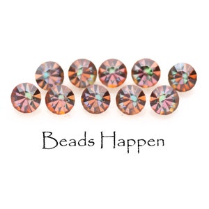May include: Ten iridescent, faceted, round, glass beads in shades of brown, orange, and green. The beads are arranged in a semi-circle on a white background. The text "Beads Happen" is printed below the beads.