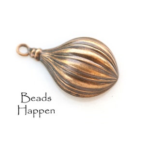 Può includere: Un perno di metallo color bronzo con una texture a coste e un anello nella parte superiore. Il perno ha la forma di una lacrima.