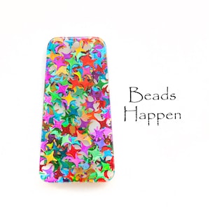 Könnte beinhalten: Ein rechteckiger, transparenter Harz-Anhänger mit einem bunten Konfetti-Design in Sternform. Der Text "Beads Happen" ist in Schwarz unter dem Anhänger geschrieben.