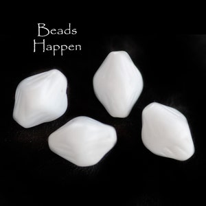 May include: Four white, faceted, plastic beads. The beads are shaped like a diamond with rounded edges. The beads are arranged in a semi-circle on a black background.