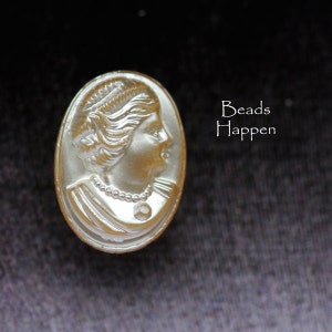 May include: A white cameo bead featuring a raised image of a woman's face. The bead is oval shaped and has a pearl necklace around the woman's neck.