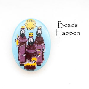 May include: A blue oval-shaped Christmas ornament with a depiction of the three wise men and a star. The ornament has the words "Beads Happen" printed on it.