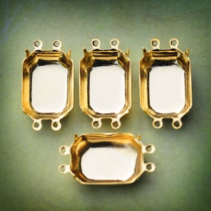 May include: Four gold-toned metal settings for bezel settings. Each setting has a rectangular shape with rounded corners and four loops on the sides.