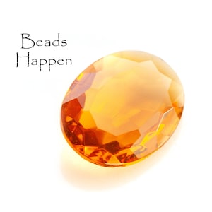 Puede incluir: Una gran cuenta de vidrio de forma ovalada, de color ámbar. La cuenta tiene un diseño facetado y es translúcida.