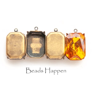May include: Three gold-toned metal settings with a single clear orange gemstone in the fourth setting. The settings have a beveled edge and a loop at the top. The text "Beads Happen" is printed below the settings.