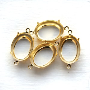 May include: Four gold-toned oval-shaped metal settings for jewelry making. The settings have a smooth, shiny finish and are designed to hold a stone or other embellishment.