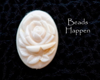 May include: A white carved rose bead with a detailed design. The bead is oval shaped and has a smooth, polished finish. The text "Beads Happen" is visible in the background.
