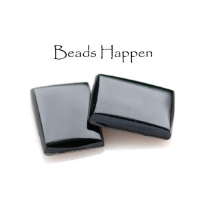 May include: Two black rectangular glass tiles with a glossy finish. The tiles are slightly angled and overlapping. The text "Beads Happen" is written in black above the tiles.