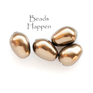 May include: Four gold-colored pearlescent beads, each with a smooth, rounded surface. The beads are arranged in a cluster on a white background. The text "Beads Happen" is written in black above the beads.
