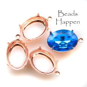 May include: Four gold-tone oval-shaped metal settings with prongs and a loop for hanging. One setting is filled with a bright blue faceted gemstone.