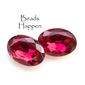 May include: Two oval-shaped, faceted, red glass beads. The beads are on a white background.