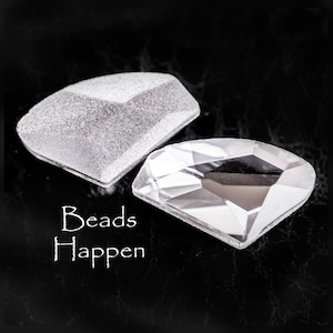 May include: Two clear glass beads, one with a frosted finish and the other with a smooth, faceted surface. The beads are on a black background with the text "Beads Happen" written below.