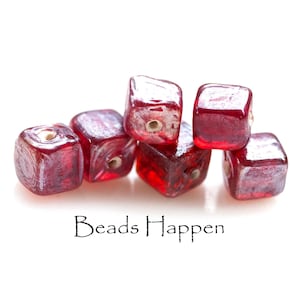May include: Five translucent red cube-shaped beads with a metallic silver finish on the edges and a central hole. The text "Beads Happen" is printed in black below the beads. The beads have a glossy, reflective surface and a square shape.