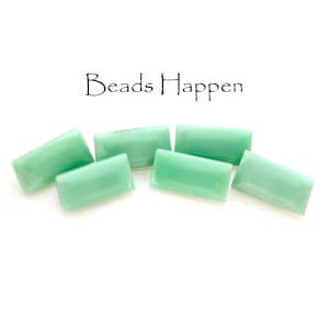 May include: Five light green, rectangular, faceted gemstone beads. The beads are arranged in a semi-circle on a white surface. The text "Beads Happen" is visible above the beads.