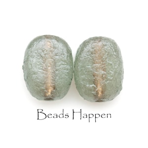 May include: Two light green glass beads with a textured surface. The beads have a gold-colored core running through the center. The text "Beads Happen" is printed below the beads.